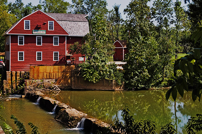 River with green foliage and red barn shaped mill building