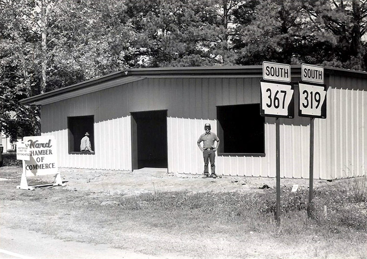 White man standing outside building with metal siding and sign