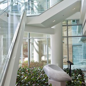 Stone sculpture of abstract shape placed amid greenery indoors next to staircase