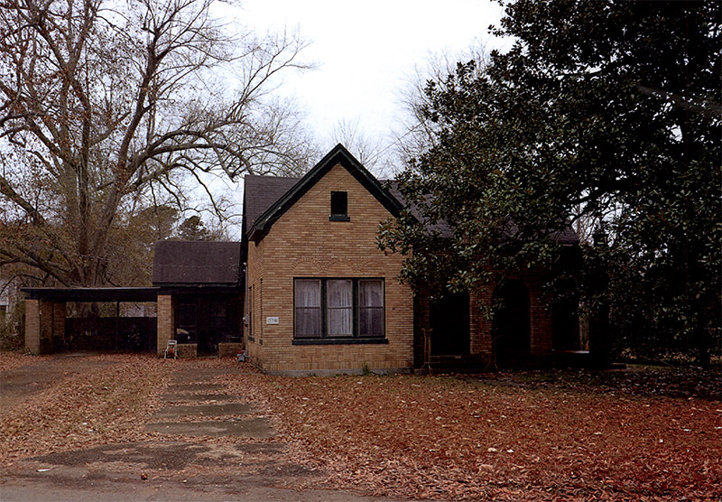 Brick house with covered porch and car port on leaf covered lawn