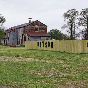 Multistory rusted barn with wooden fence with large letters on it saying "Watson"