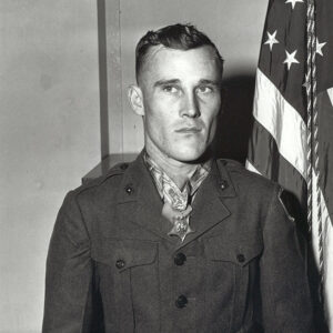 Young white man wearing Medal of Honor standing in military uniform with American flag behind him