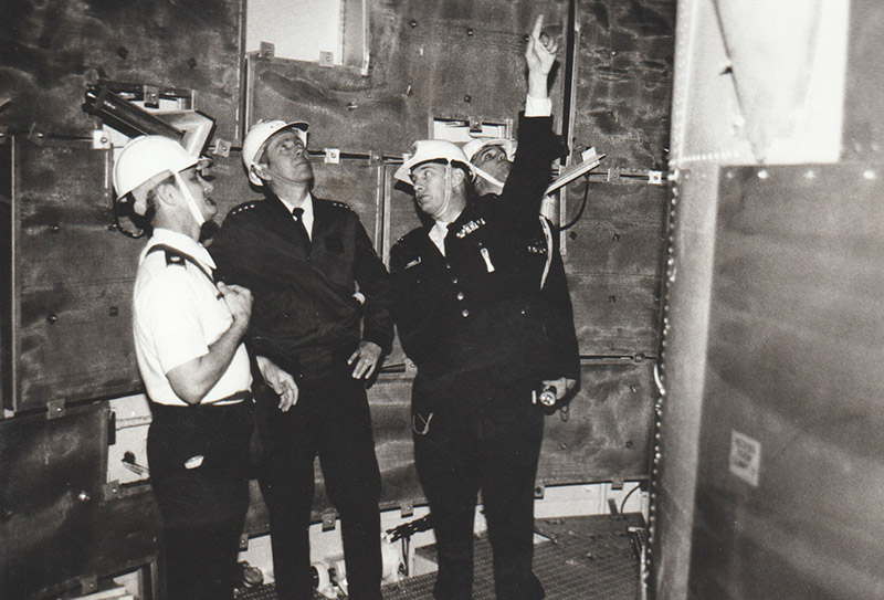 Three white men in helmets inside a complex