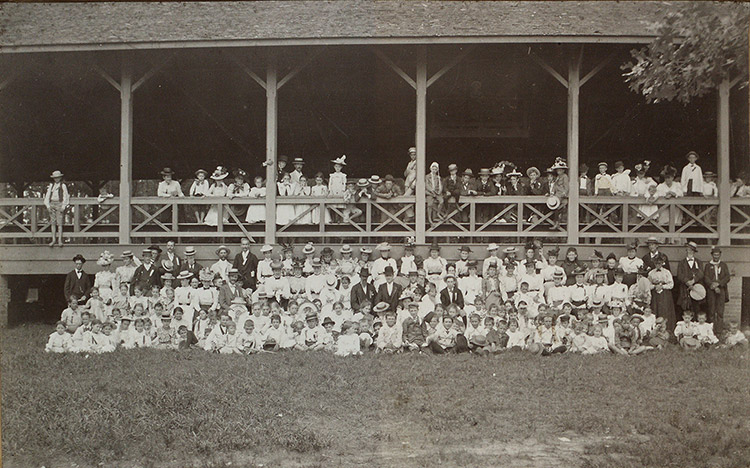 Group of white men women and children gathered at large outdoor pavilion