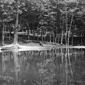 Man in boat on park pond with trees reflected in the water
