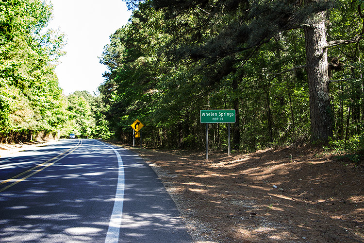 Green "Whelen Springs" road sign on right side of tree-lined two-lane highway