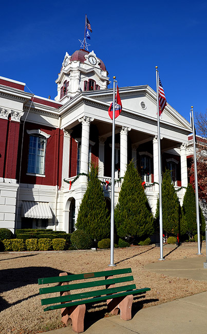 Close-up of multistory building with clock tower and covered entrance with columns and three flag poles in front yard