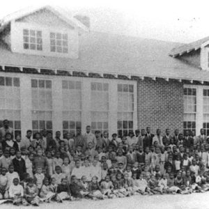 African-American children and faculty posing together outside multistory brick building