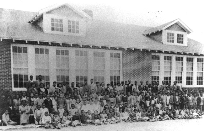 African-American children and faculty posing together outside multistory brick building