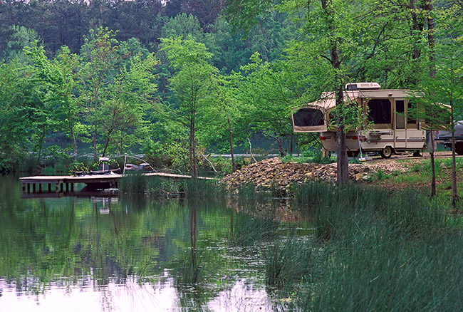 Boat dock on lake with R.V. at campsite and trees