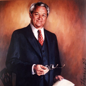 White man with in three-piece suit holding a pair of glasses