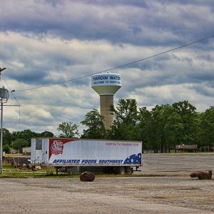 Semi-truck trailer on gravel parking lot with water tower in the background