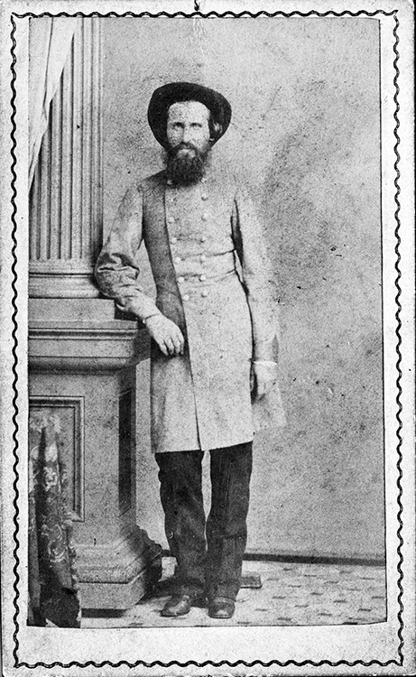 White man with long beard in hat and gray military uniform leaning on a column