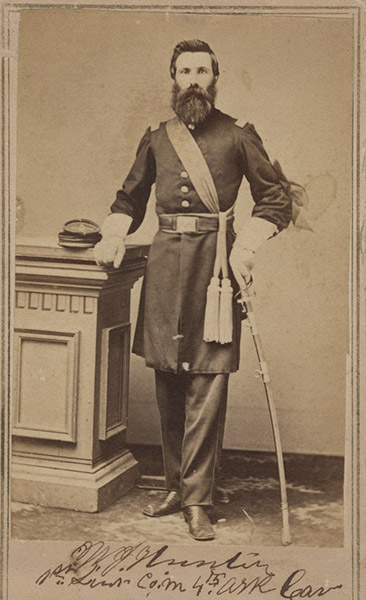 White man with long beard standing in military uniform with sword in hand