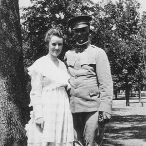 White man in military uniform standing with white woman in dress with trees behind them