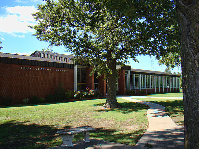 Single-story brick and glass library building and trees with walking path