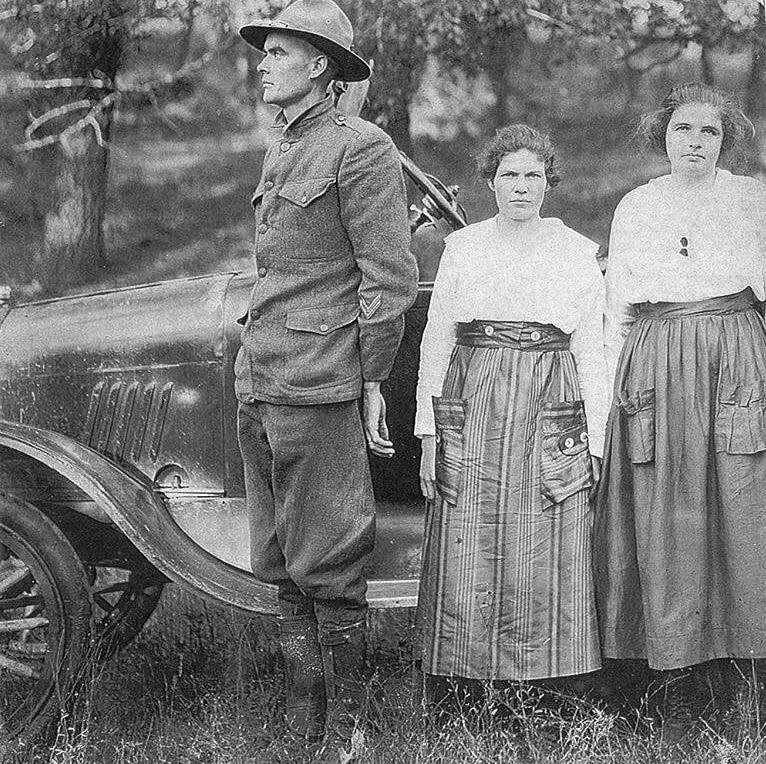 White man in military uniform with two white women and car