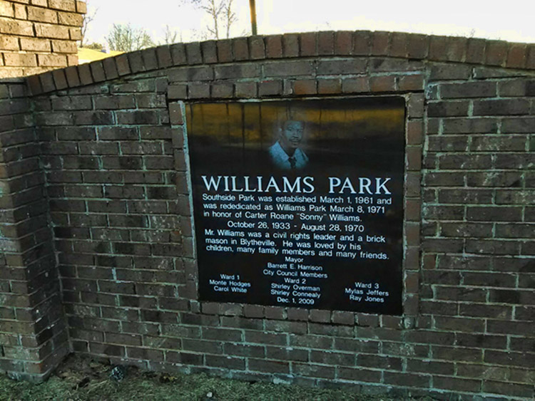 Brick wall with "Williams Park" plaque and image of an African-American man on it with white text
