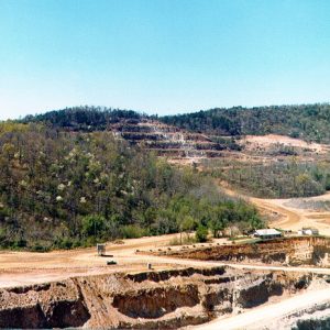 Single-story building at entrance to open pit mine with tree covered multilevel mine wall in the background