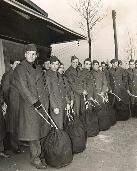 Group of young white men in military coats and caps standing with duffel bags