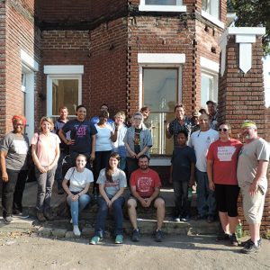 Mixed group of men and women in front of multistory brick house