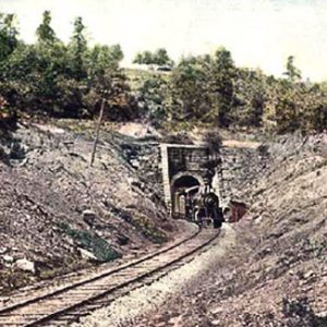 Steam locomotive coming through stone tunnel on tracks