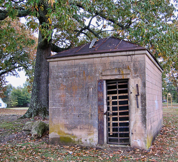 Small brick building with metal roof and bars on the door