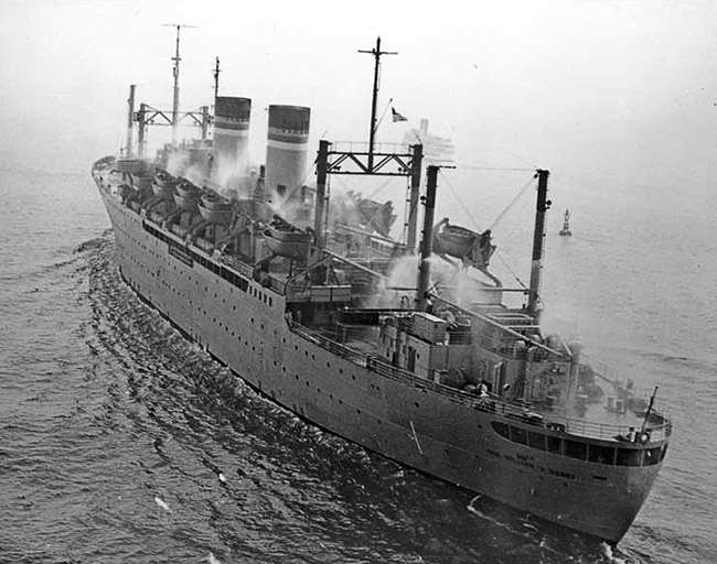 Large ship with two smoke stacks at sea with sprinkler system operating