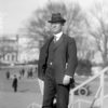White man in suit and hat standing on steps outdoors