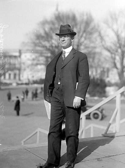 White man in suit and hat standing on steps outdoors