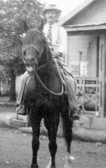 Old white man on horseback with building with covered porch behind him