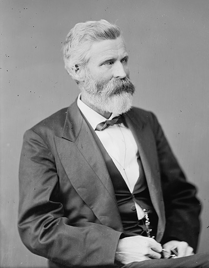 White man with beard sitting in suit and bow tie