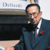Old white man with glasses in suit and tie standing outside "Dillard's" store building