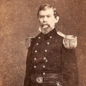 White man with mustache standing in military uniform with sword in his left hand and hat in his right hand