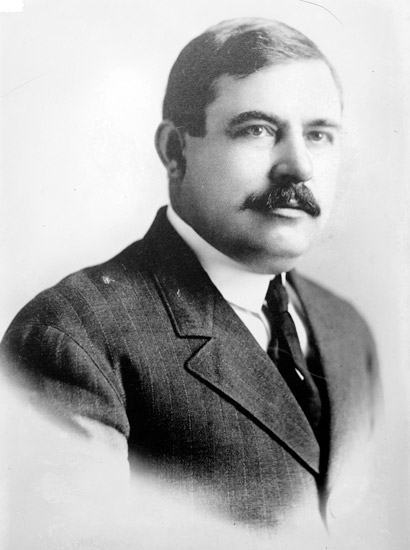 White man with dark hair and mustache in suit jacket and tie