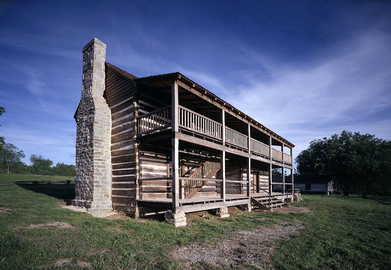 Two-story log cabin with stone chimney under blue skies
