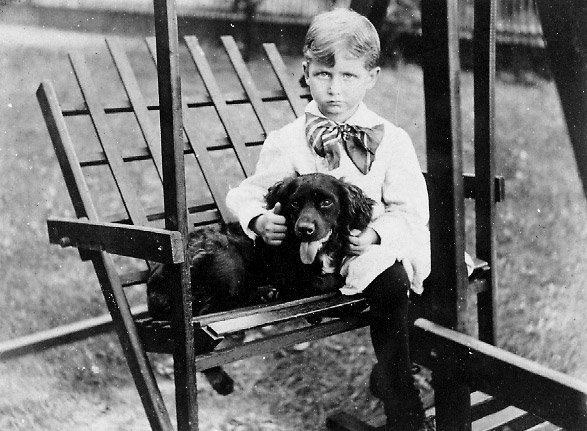 White boy with large bow tie and dog sitting in a wooden swing
