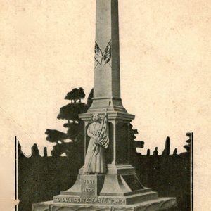 Stone obelisk shaped monument and statue of soldier with flag and text on post card