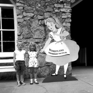White boy and girl with Alice in Wonderland cutout and stone building