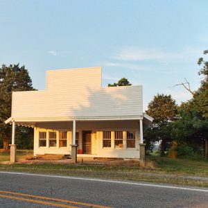 Single-story storefront with covered porch on two-lane road