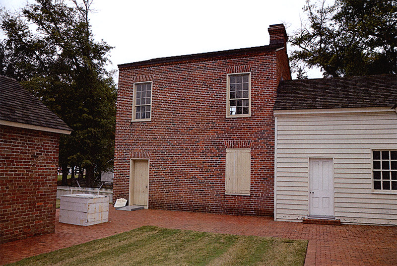 Rear view of two-story brick building adjoining single-story structure with wood siding on museum grounds
