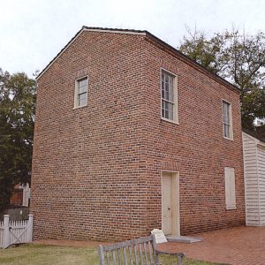 Side view of two-story brick building adjoining single-story wooden structure on museum grounds