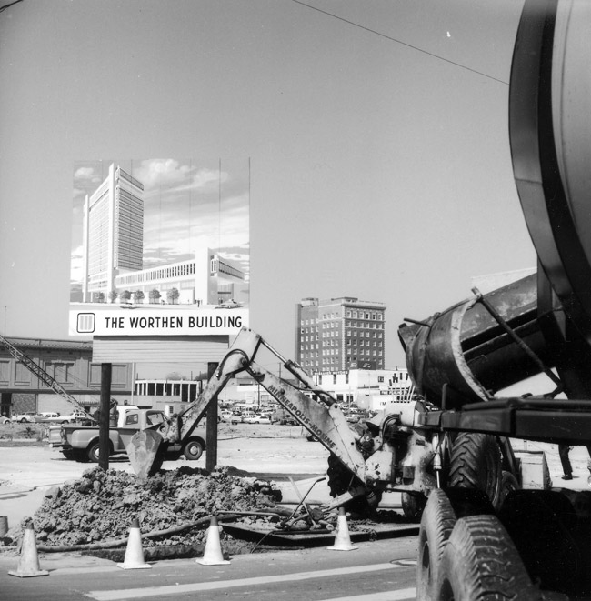 Construction site with tall building in the background and sign advertising the coming building with truck and construction equipment in the foreground