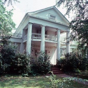 Two-story house with attic with covered porch and balcony with four columns and bushes in front