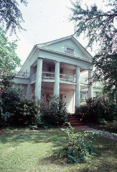 Two-story house with attic with covered porch and balcony with four columns and bushes in front