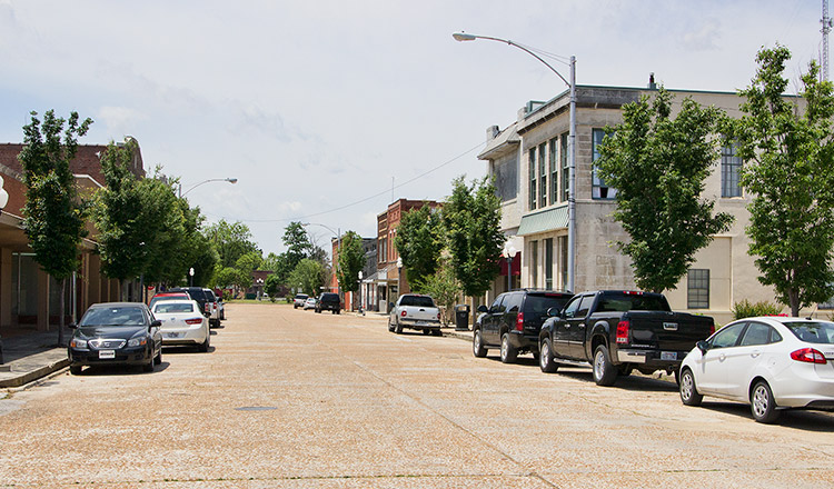 Street with two-story brick storefronts parked cars and trees