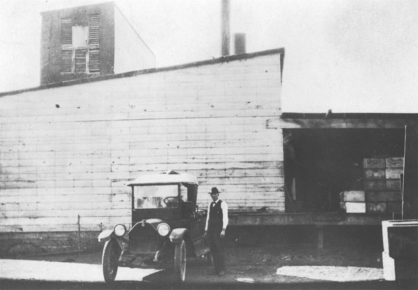 Man in suit with car outside building with smokestack and loading dock