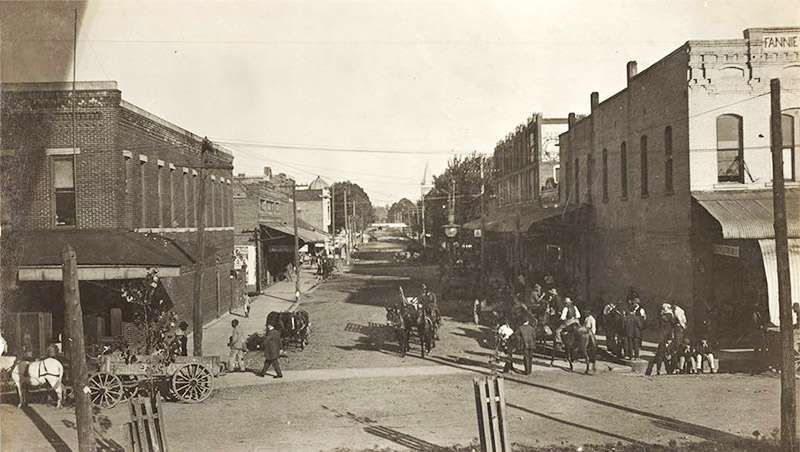 Horse drawn wagons and people walking on town street