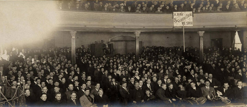 White crowd in auditorium with X-Ray banner as seen from stage