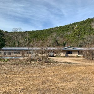 Motel building on dirt road with tree covered hill behind it